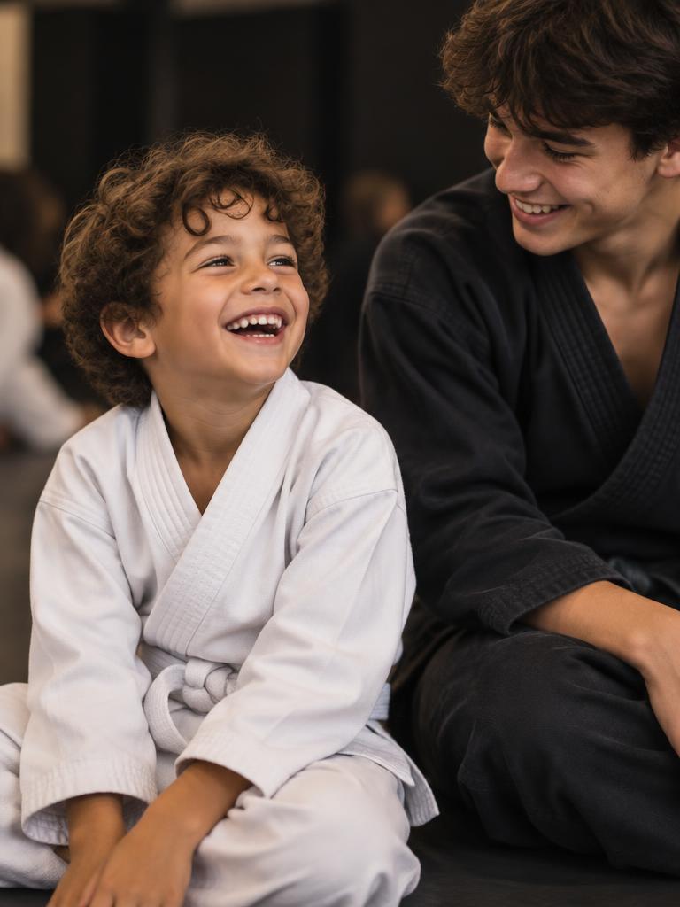 Joyful young boy in a white gi sitting beside an older student in a dark gi